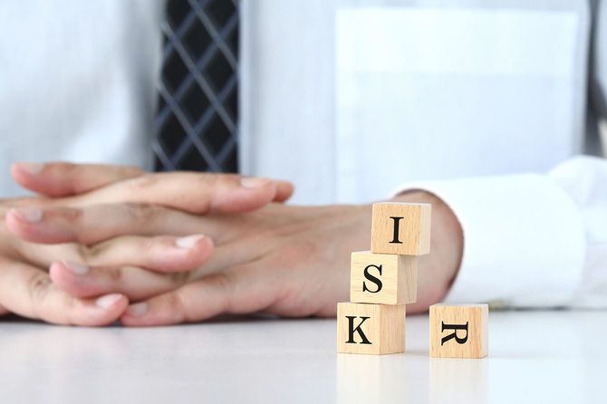 手を組んでいるビジネスマンと、「RISK」と書かれた積み木