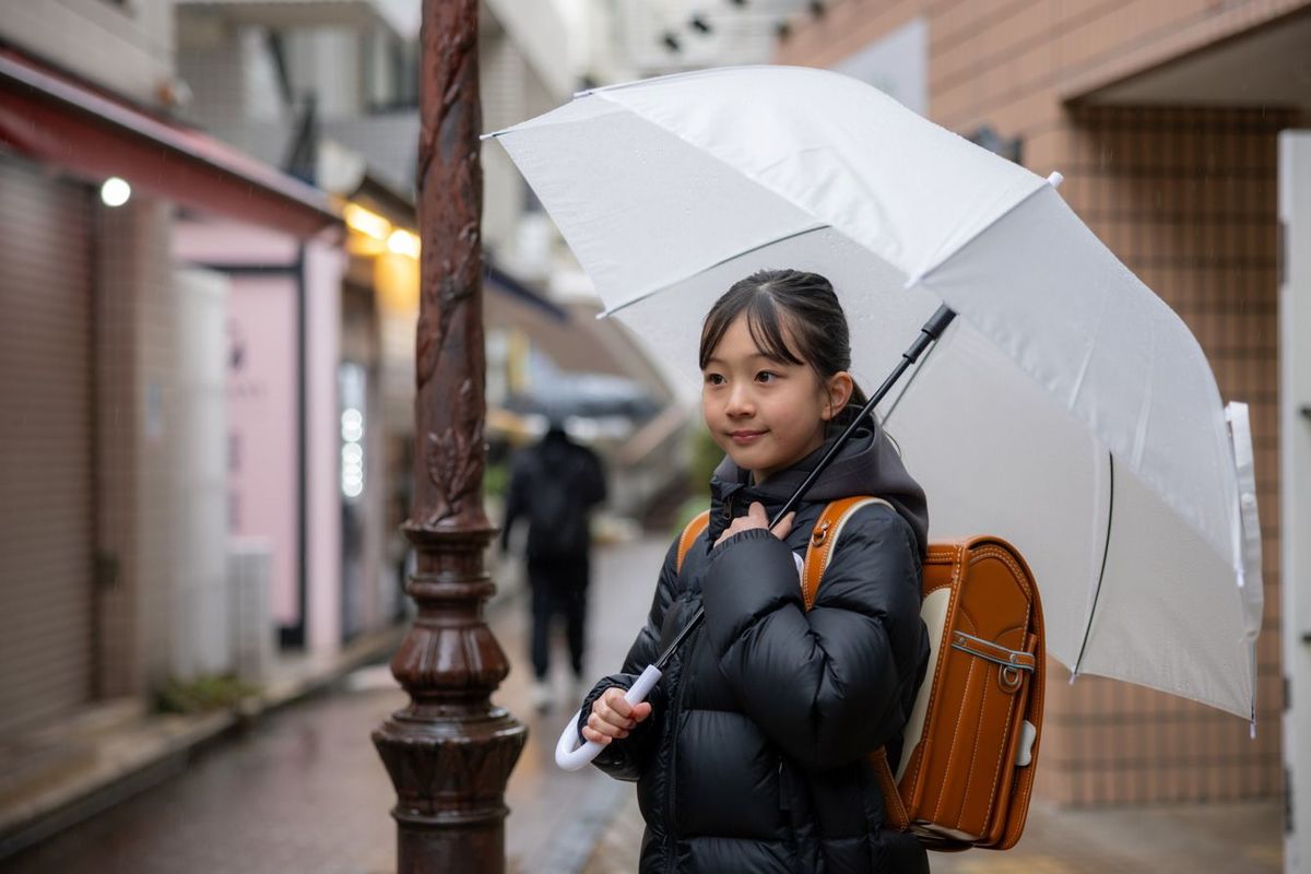 雨の日に傘をさしてランドセルを背負う日本の小学生の女の子