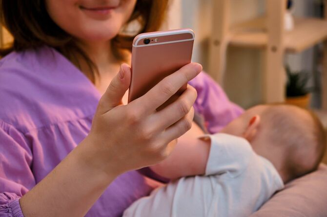 赤ちゃんを抱きながらスマートフォンを見る女性