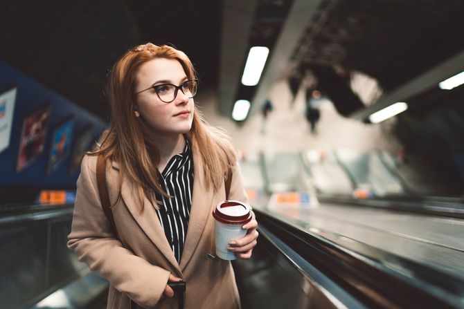 リュックサックのため、空いた手にはコーヒーを持ってエスカレーターに乗る女性