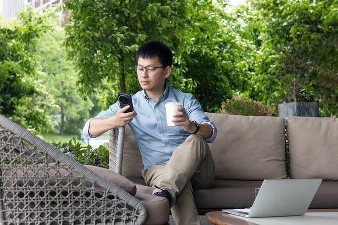 屋外のソファに座りスマートフォンを見る男性