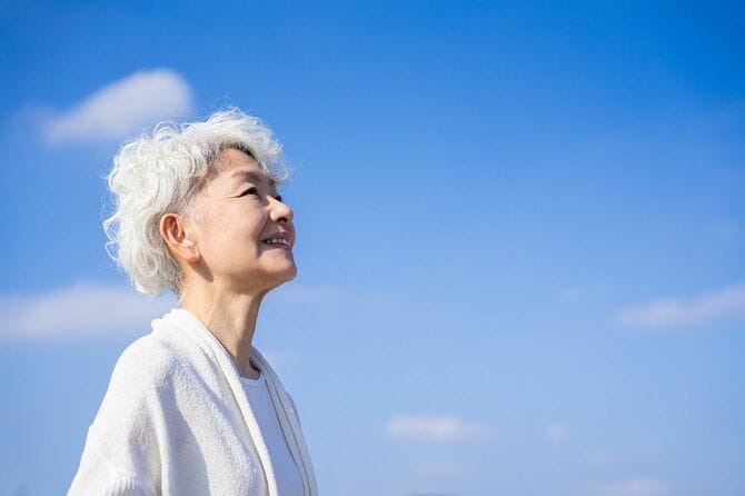 青空を見上げて立つ年配の女性