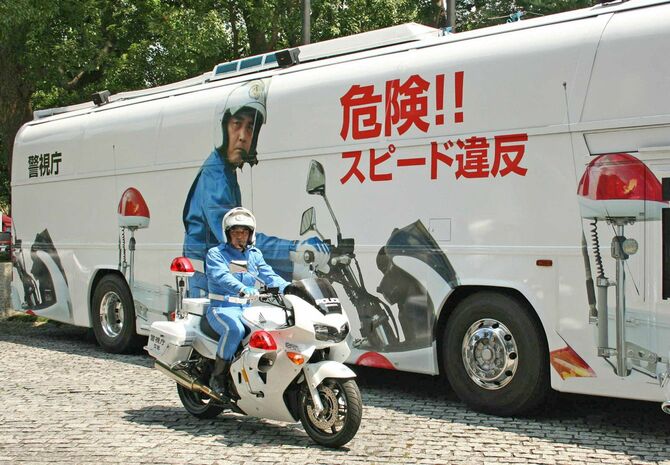 警視庁が安全運転などをアピールするため走らせる巨大な白バイの画像などを施したラッピングバス。手前はモデルとなった丸田正四郎巡査部長