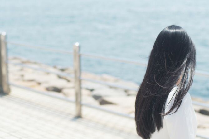 長く美しい黒髪の女性が海を見ている