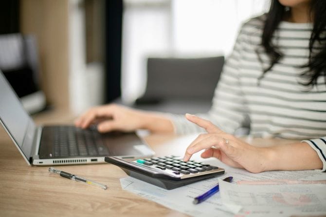 左手では電卓を使用しながら、ノートパソコンを使用する女性の手元