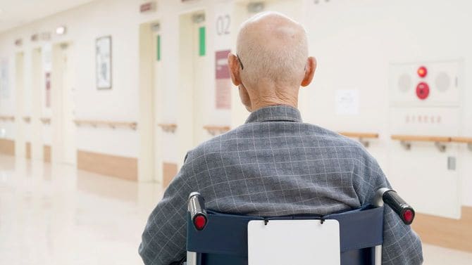 病院内を車椅子で移動する高齢男性