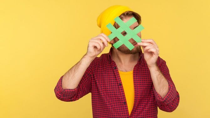 ハッシュタグサインを手で持ち、その穴からこちらを見つめる男性