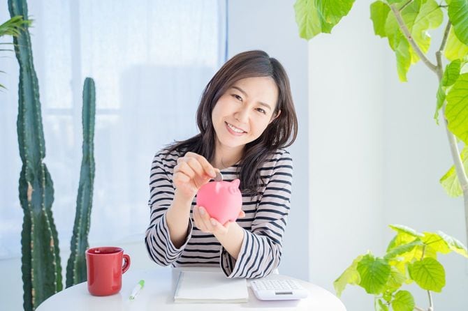 明るいリビングルームで貯金箱に硬貨を入れる女性