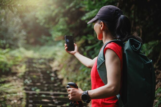 女性がスマートフォンを使って秋の森山でハイキングを撮影