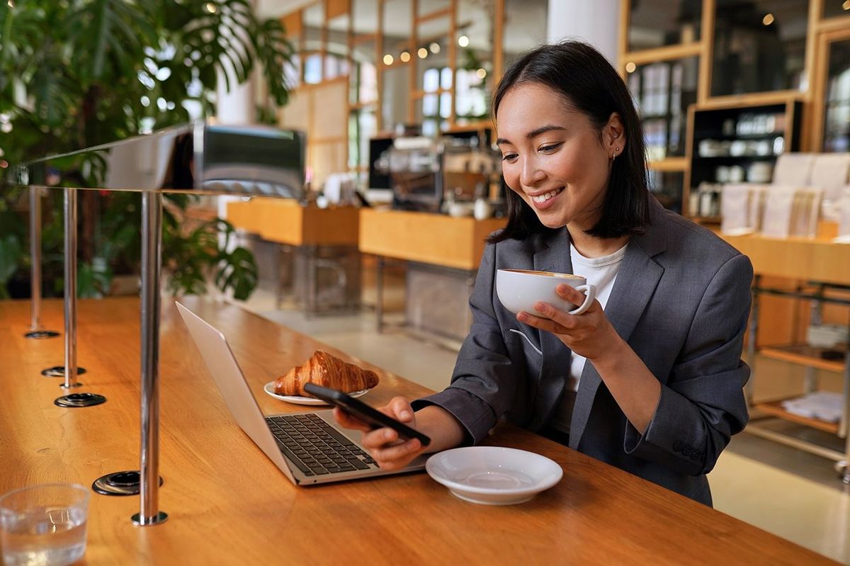 カフェで電話を使ってコーヒーを飲みながらスーツを着た若いアジア人ビジネスウーマン