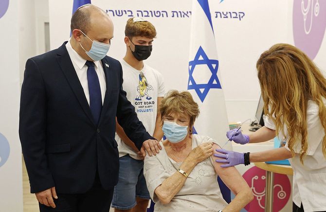 新型コロナウイルスワクチンの3回目の接種を受けるイスラエルのベネット首相（左）の母親（中央）