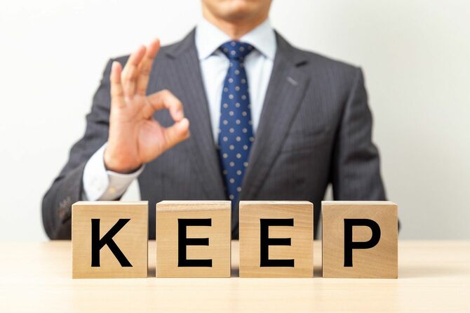 「KEEP」と書かれたブロックを持ってOKポーズをとるビジネスマン