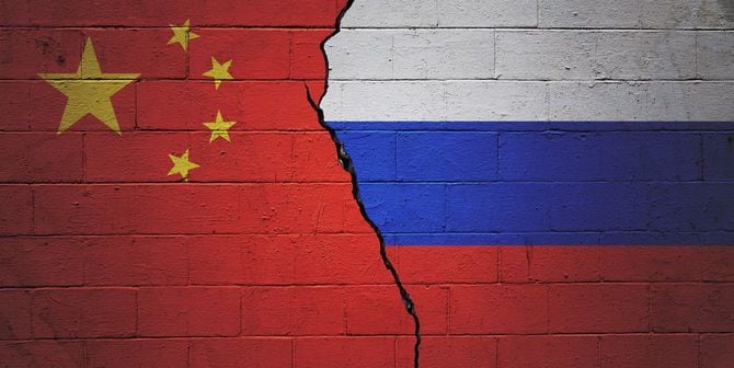 ひび割れた壁面に描かれた五星紅旗とロシアの国旗