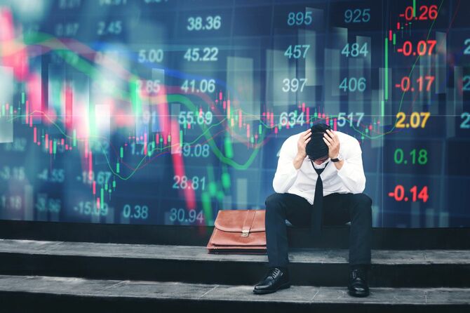 株価掲示板の前で頭を抱えて座り込んでいる男性