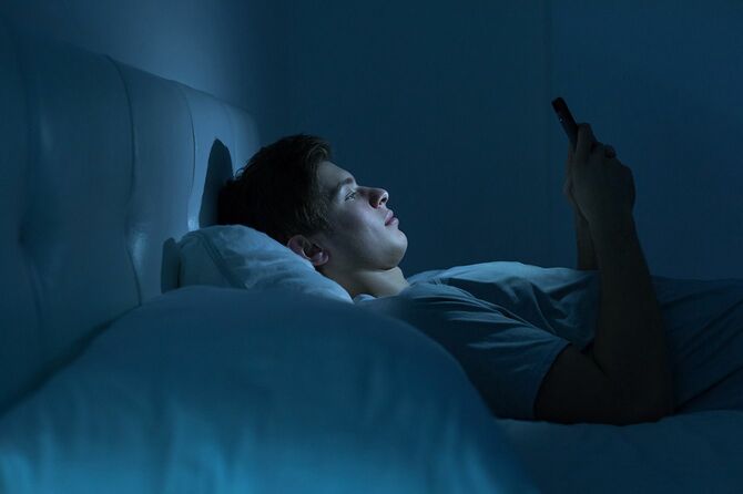 夜、ベッドに横になりスマホを見ている男性