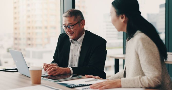 オフィスでラップトップを開いて談笑する中高年ビジネスマン