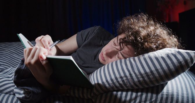 ベッドに横たわり、ノートにメモを取る女性