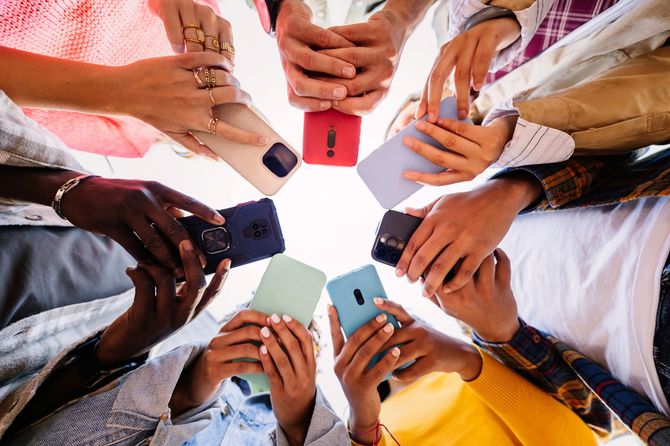 外で一緒にスマートフォンを使う若い学生グループ
