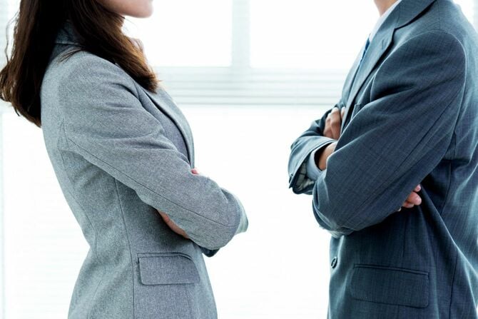 腕を組んで向き合う二人のビジネスパーソン