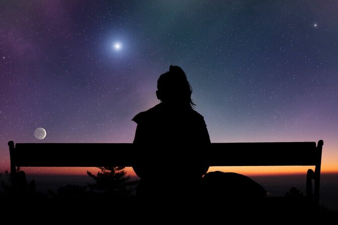 屋外に座り、星を見ている女性のシルエット