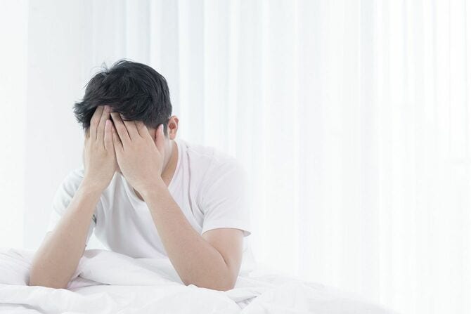 ベット上で手で顔を覆う男性