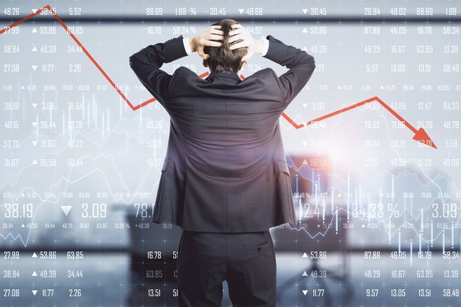 急落する株価チャートの前で頭を抱えている男性の後ろ姿
