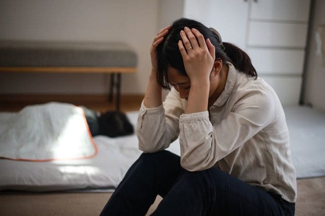 眠っている子供のそばで頭を抱える母親