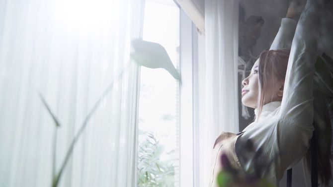 窓際の朝日に浴びながら伸びをする女性