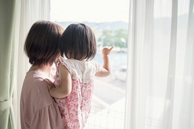 母親に抱きかかえられて窓の外を見る赤ちゃん