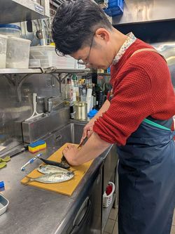 マルカマの厨房でメアジの下処理を行う筆者。刺身と湯煮用は頭と内臓を除去し、塩焼き用は頭を残します（筆者撮影）