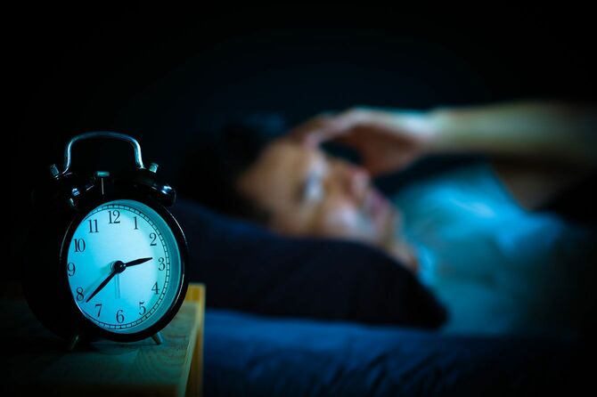 ベッドに横になっている男性と目覚まし時計