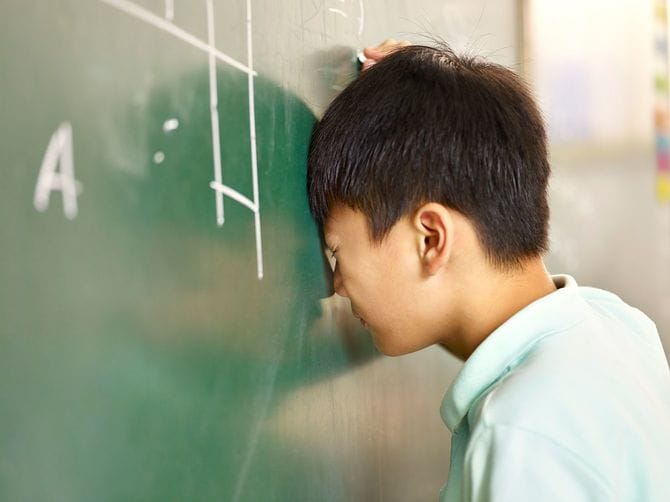 男の子が黒板で問題を解きながらいらいらして頭を打ちつける