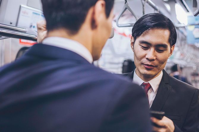 電車の中で向かい合って会話をする2人のビジネスマン