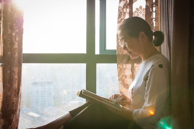 夕暮れ時に窓際で本を読むシニア女性