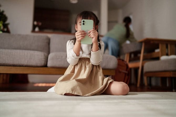 家で床に座ってスマートフォンを使う幼い子供